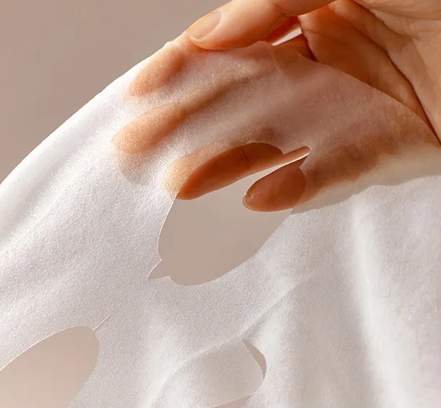 Hand applying a white sheet mask to skin