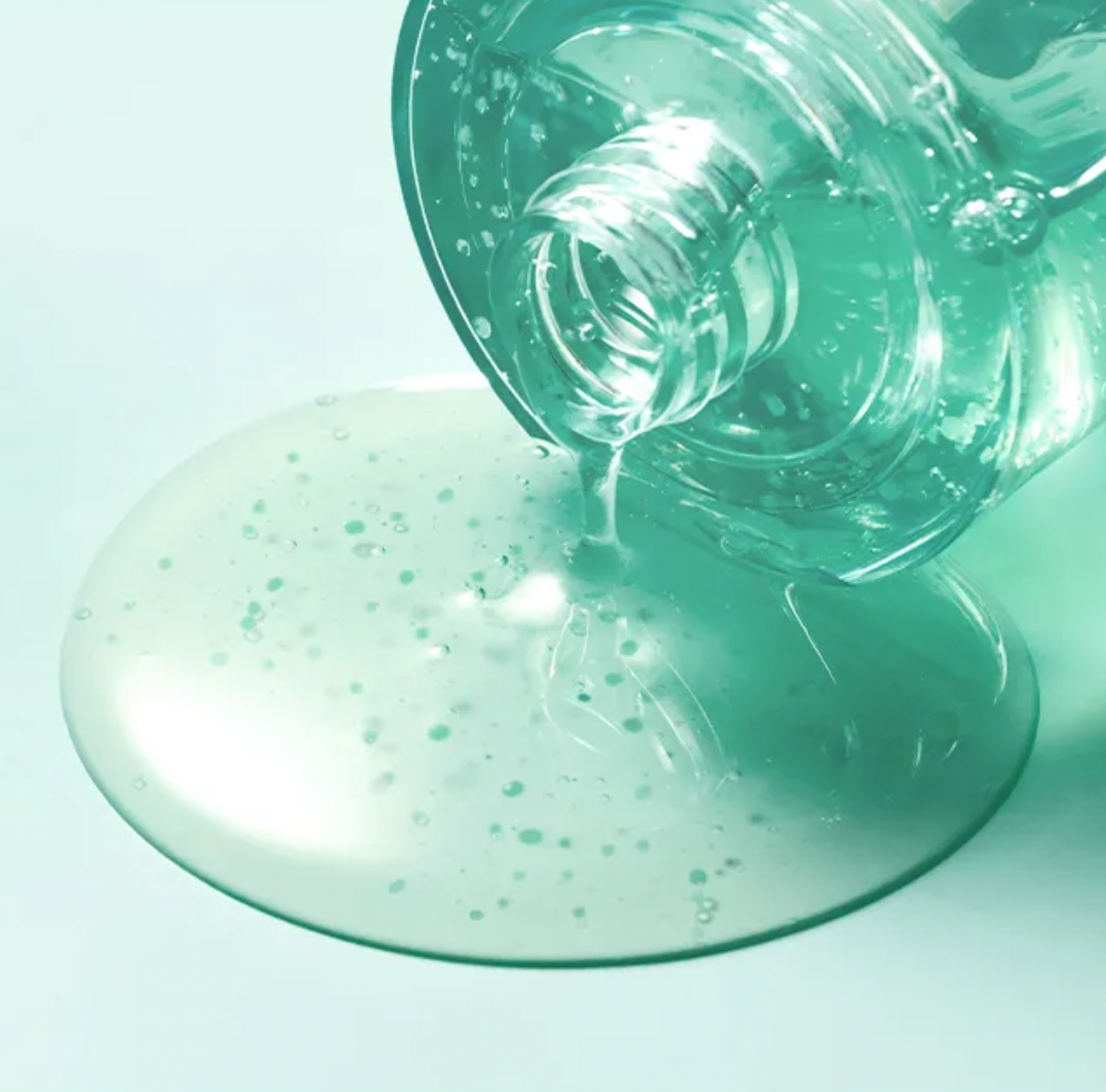 Clear bottle pouring green serum onto a light green surface