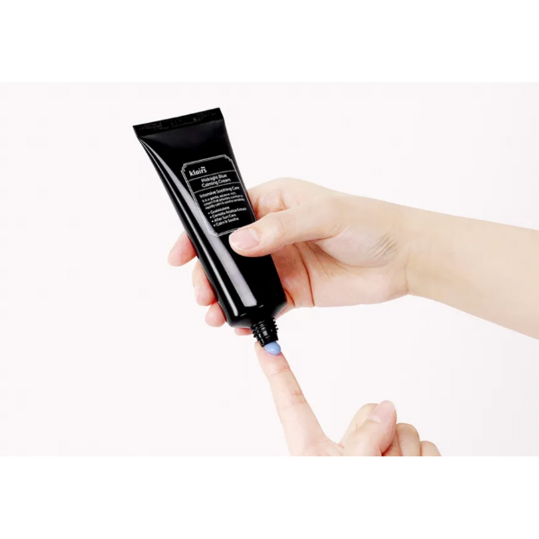 Hand holding a black cosmetic tube with visible text on a white background