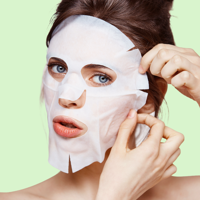 Woman applying a white face mask against a light green background