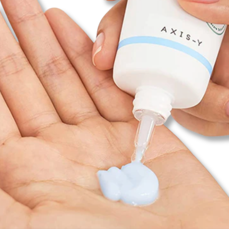 Hand holding a tube labeled 'AXIS-Y' with a small amount of cream being squeezed onto the palm.