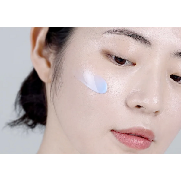 Close-up of a woman's face with a small amount of cream on her cheek against a neutral background