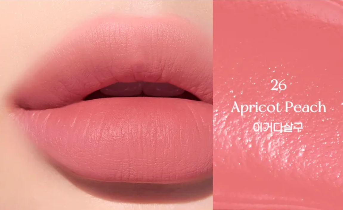 Close-up of a pink lip color swatch with '26 Apricot Peach' text on a beige background.