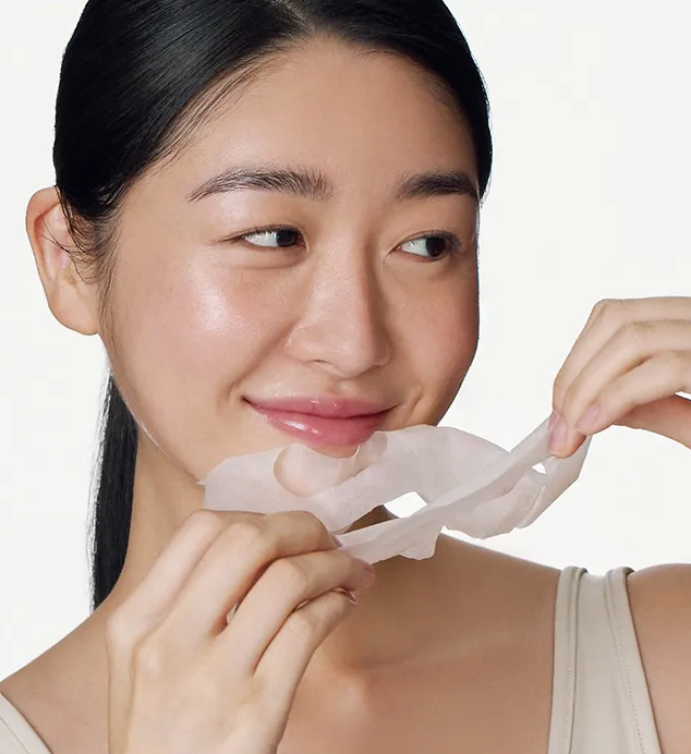 Woman applying a white patch to her face against a plain background