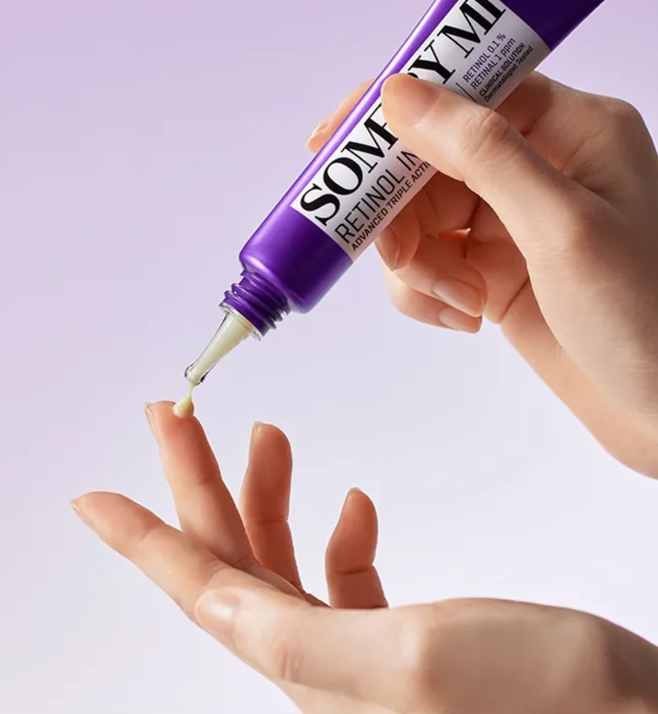 Hand holding a purple cosmetic tube labeled 'SOMYUN' with a dropper, against a light purple background.