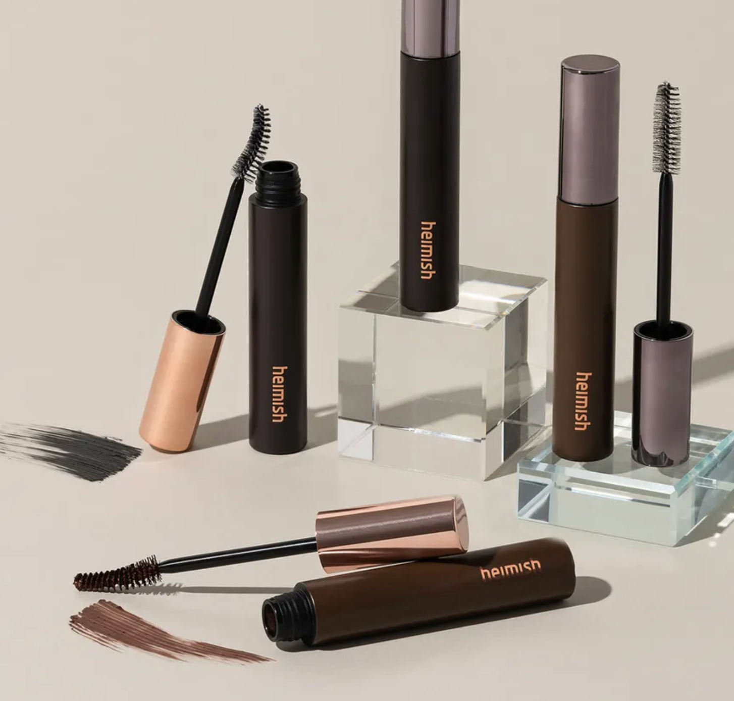 Heimish mascara and brow products on a neutral background