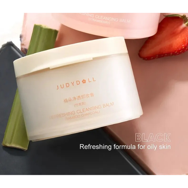 JudyDoll cleansing balm container with aloe vera leaf and strawberry on a black background